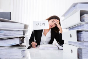 Young Unhappy Businesswoman Sitting And Holding White Flag With The Text Help In Office