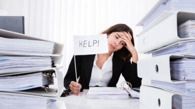 Young Unhappy Businesswoman Sitting And Holding White Flag With The Text Help In Office